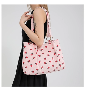 Detail of pink corduroy tote bag featuring red strawberry prints and gold ring handles