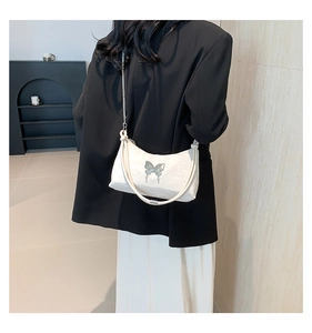 Detailansicht der cremefarbenen Tasche mit silbernem Metallschmetterling und Kette