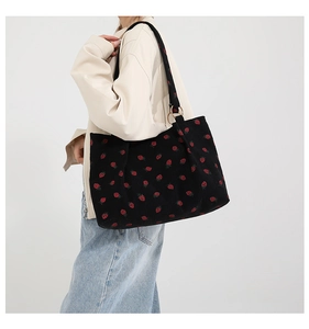 Detail of black corduroy tote bag with red strawberry embroidery and golden metal ring