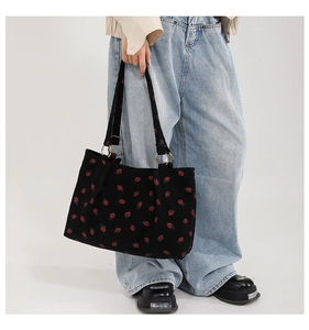 Close-up of black corduroy tote bag featuring red strawberry embroidery and gold hardware