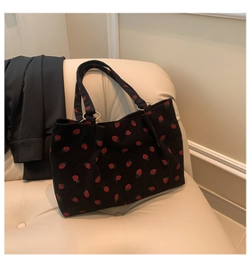 Detail of black corduroy tote bag with red strawberry print and gold metal ring handle