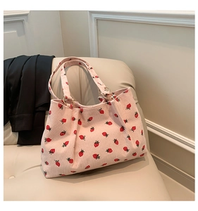 Detail of pink corduroy tote bag featuring red strawberry prints and golden hardware