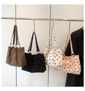 Detail of four colorful corduroy tote bags with strawberry prints hanging on a rack