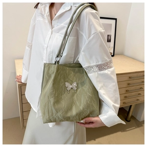 Détail du sac cabas plissé vert clair avec breloque papillon argentée sur dentelle blanche