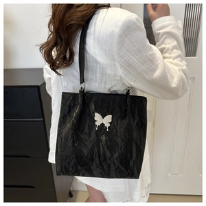 Détail du sac cabas noir avec texture plissée et emblème papillon blanc élégant