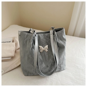 Détail du sac cabas argenté avec texture plissée et pendentif papillon en métal argenté