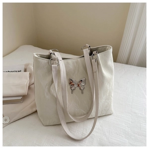 Détail du sac cabas blanc texturé avec breloque papillon argentée et anses vintage
