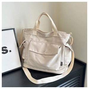 Détail d'un sac cabas en toile avec poches latérales et étiquette tendance sur tissu blanc cassé