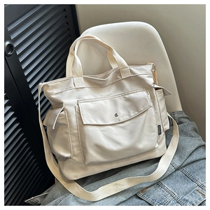 Detail view of beige canvas tote bag showing side pockets and fashion label on the chair