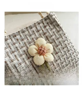 Dettaglio macro della trama in tweed e del fiore in tessuto 3D sulla borsa a secchiello