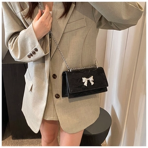 Détail d'un petit sac bandoulière noir avec nœud argenté et fine chaîne métallique
