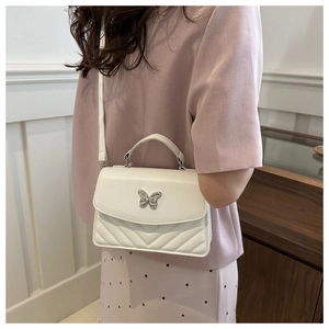 Detail of white quilted crossbody bag with golden butterfly clasp shown on model