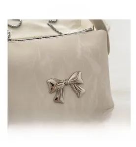 Détail d'un sac à main en cuir PU crème avec un nœud en métal argenté et une chaîne