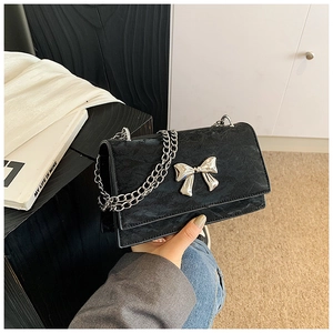 Détail d'un sac bandoulière en daim noir avec nœud en argent et chaîne