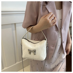 Detail of white pleated handbag with silver bow accent and elegant metal chain strap