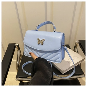 Detail of light blue crossbody bag featuring a golden butterfly clasp and V-shaped quilting