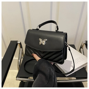 Detail of black crossbody bag featuring silver butterfly buckle and chevron stitching