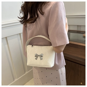 Detail showing white handbag with silver bow accent and chain strap worn by a model