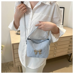 Detail of light blue pleated handbag featuring a gold metal bow and elegant chain strap