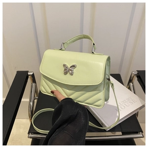 Detail of light green quilted handbag with silver butterfly buckle on black leather chair