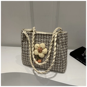 Dettaglio della borsa tote in paglia con trama in tweed e ciondolo floreale