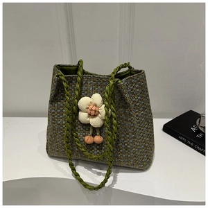 Dettaglio della borsa tote intrecciata con fiori 3D e manici in corda verde su piedistallo