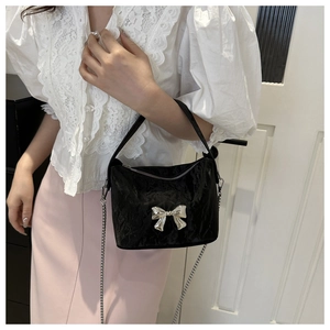 Détail du sac seau en cuir verni noir avec nœud en métal argenté sur un mannequin