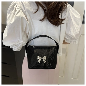 Close-up of black pleated crossbody bag with silver bow accent and chain strap worn by model
