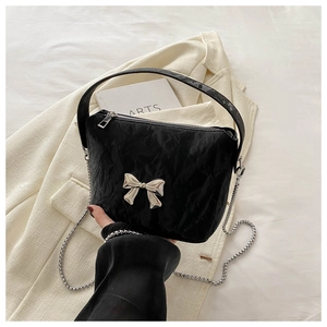 Detail of black pleated handbag featuring a silver metal bow and detachable chain strap