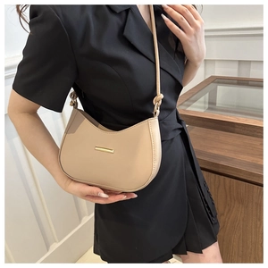 Detail of a beige half-moon shoulder bag with a gold metal clasp worn with a black dress