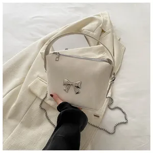 Detail of creamy white leather tote featuring a silver metallic bow and chain strap