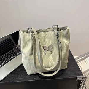 Sac fourre-tout texturé vert pistache avec papillon argenté sur bureau de travail