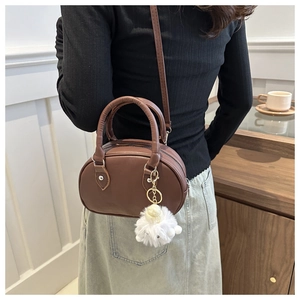 Borsa a tracolla ovale in pelle marrone con ciondolo di peluche bianco su modella