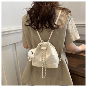 Detail view of beige drawstring bucket backpack with chain strap and plush ball charm