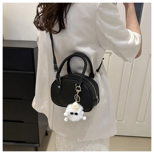 Détail d'un sac bandoulière noir ovale avec une breloque monstre en peluche blanche