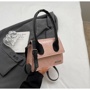 Detalle de bolso bandolera rosa y negro con logo metálico sobre fondo gris elegante