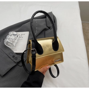 Detalle de un mini bolso dorado con asa negra y placa de logo metálica de JINGPIN