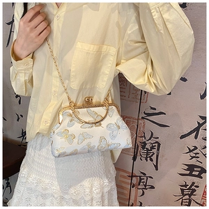 Détail de broderie papillon doré sur un sac vintage en soie blanche avec chaîne dorée
