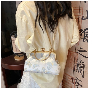 Détail d'un sac à broderie beige avec poignée dorée et motifs papillons bleus