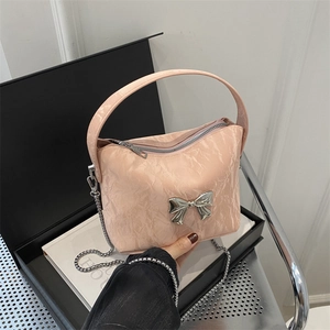 Pink pleated crossbody bag with silver bow accent and metal chain in a gift setting