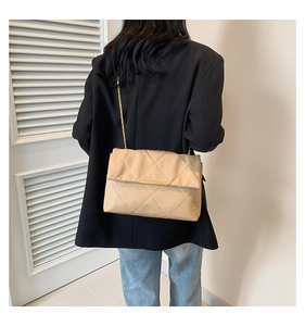 Dettaglio borsa trapuntata beige con catena dorata su blazer nero e jeans blu