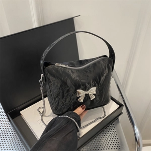 Elegant black pleated handbag with silver bow detail and chain strap on a gift box