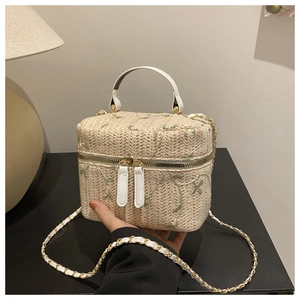 Detailed view of beige straw box bag with floral embroidery and white leather handle