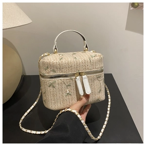 Detail of floral embroidery on a beige woven straw box bag with gold chain strap
