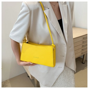 Détail d'un sac sous le bras jaune vif à la mode sur un modèle en costume blanc