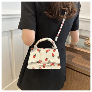 Detail van een witte mini-handtas met aardbeienprint en een stijlvol handvat riem