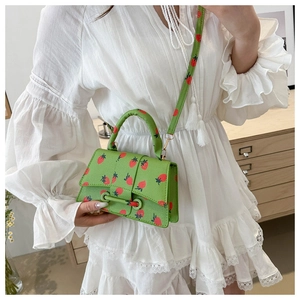 Detail van groene mini-handtas met aardbeienprint, gouden beslag en cilindrisch handvat