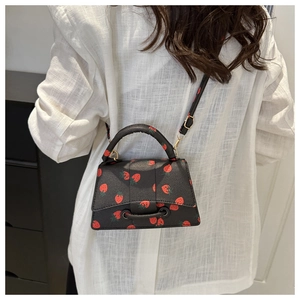 Zwarte mini crossbodytas met aardbeienprint en verstelbare schouderriem getoond op een model