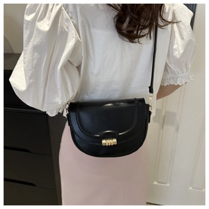 Modell trägt eine schwarze Satteltasche aus Leder mit goldener Schnalle zum weißen Oberteil