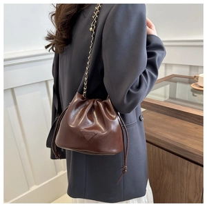 Close-up of a dark brown glossy bucket bag with woven chain strap and drawstring closure